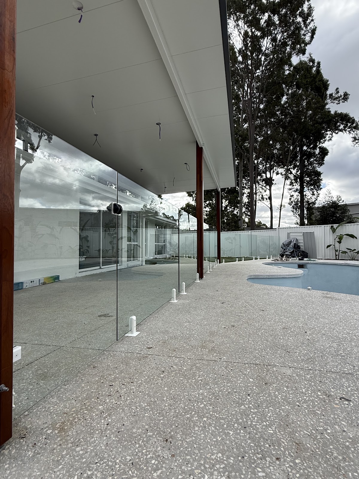 Long run of frameless glass fencing under a patio roof, pool in the distance