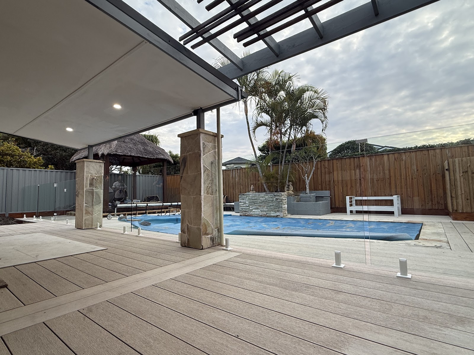 Pool deck with timber look decking and a frameless glass fence line under a pergola