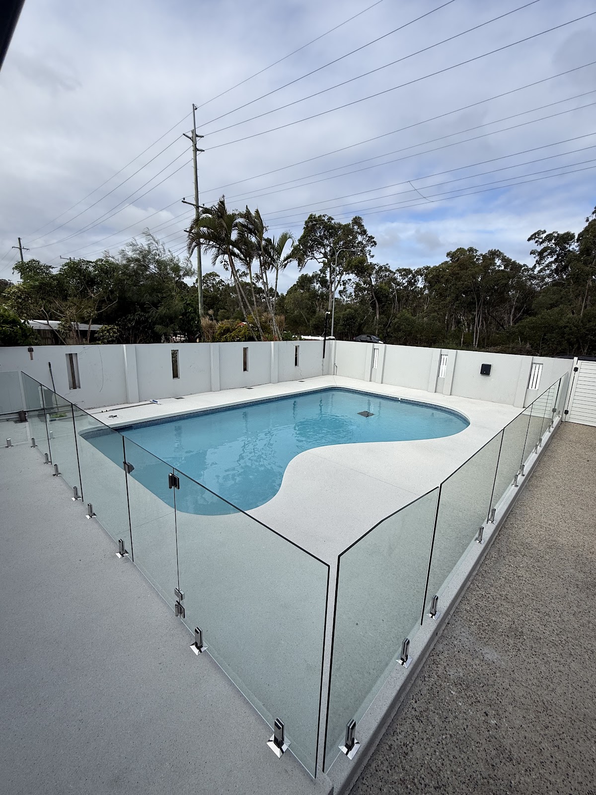 Kidney shaped pool fully fenced in frameless glass on white spigots