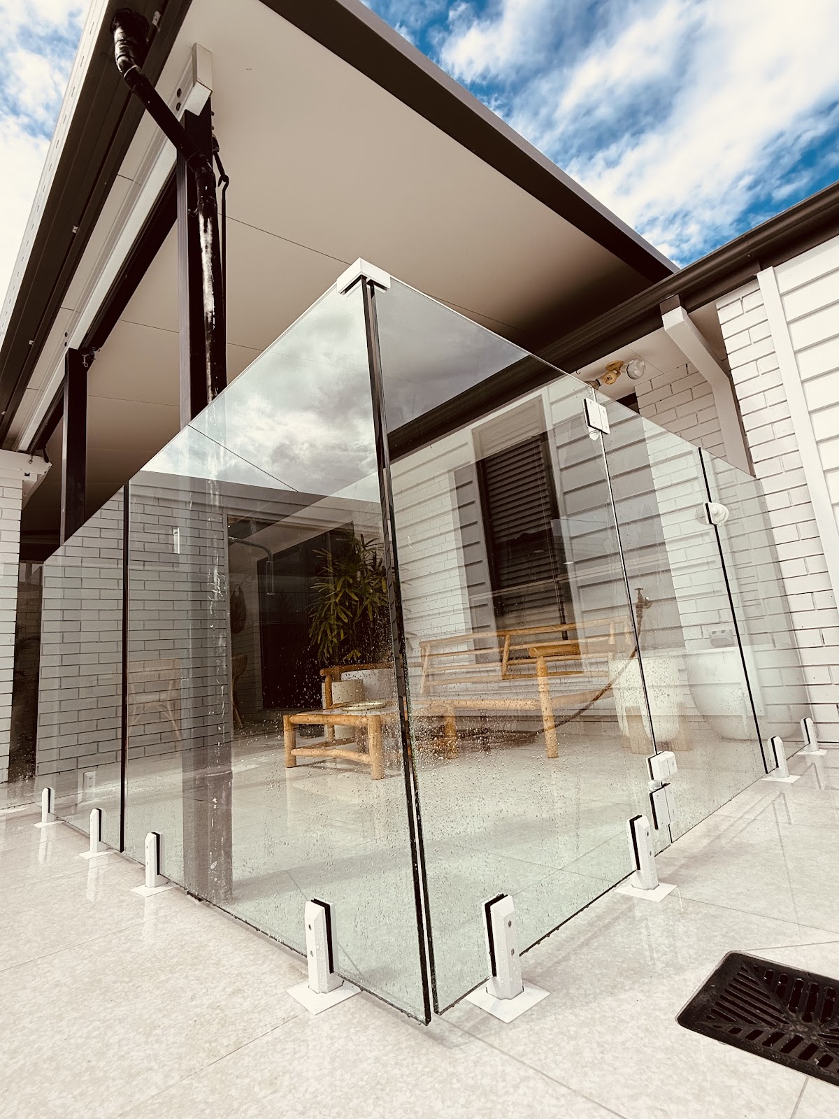 Corner of a frameless glass fence with a glass gate around a covered alfresco